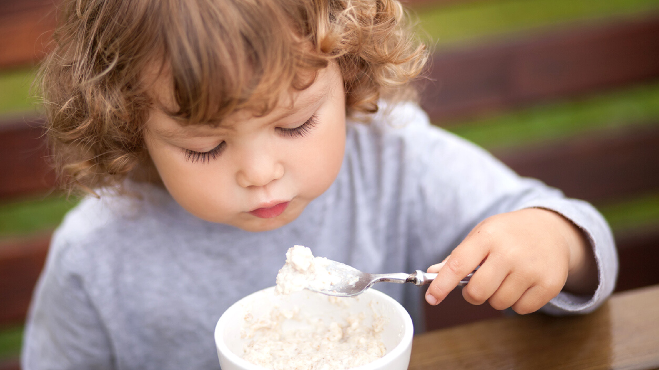 A young girl having her oatmeal outside the house.